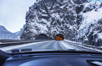 First person driver view through windshield of a car speeding toward the eastbound entrance to the US Interstate 70 Hanging Lake Tunnel which carries the expressway through parallel tunnels under the massive granite rock mountain wall of Glenwood Canyon, near Glenwood Springs, Colorado in the Rocky Mountains Range. Winter in early February, 2016.