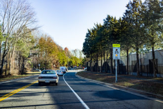 Cars waiting in traffic for Robinson Secondary School students to pass with speed limit sign