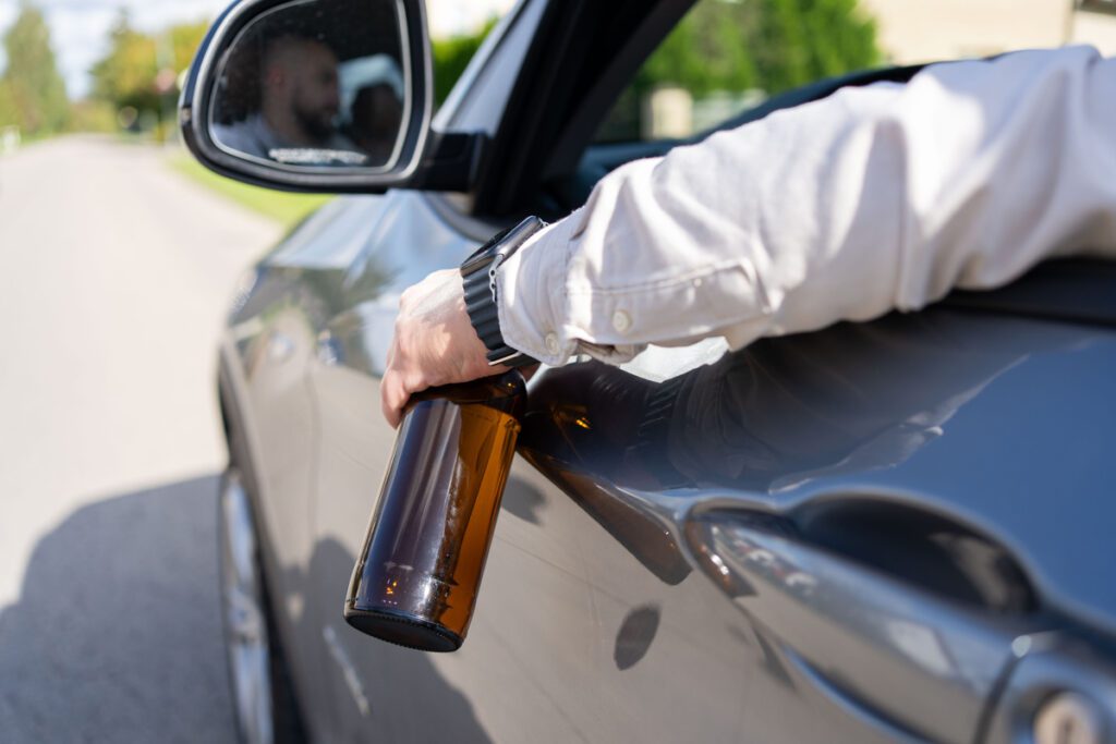 A drunken man driving a car with a bottle of alcohol in his hand. Close-up of a bottle of Alcohol in the driver hand at the wheel of car. Alcohol driving concept.